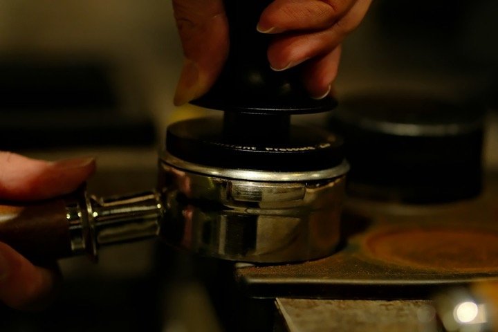 Barista care preseaza cafeaua in portafiltru cu un tamper